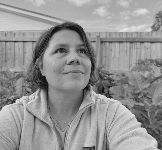 mary-hathaway-headshot-bw-apr2026 Mary Hathaway looking towards the sky, with plants and a fence behind her