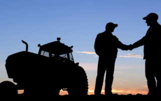 two silhouettes shaking hands in a field with a tractor behind them