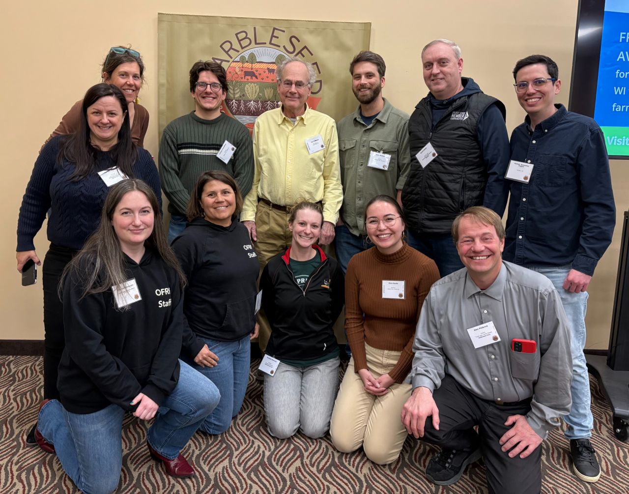 Organic researchers and OFRF staff pose in front of a Marbleseed banner at the organic conference.