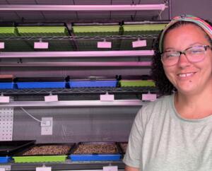Farmer Tiffany Sanders stands in front of shelves of seeded microgreens.