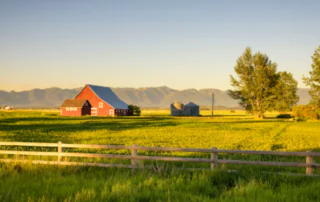sunset on a red barn with farm fields in the foreground and mountains in the background