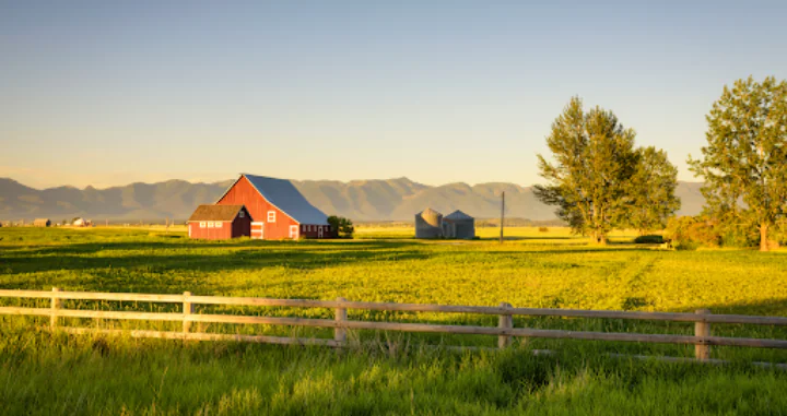 sunset on a red barn with farm fields in the foreground and mountains in the background