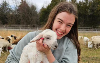 A farmer smiles holding a lamb.