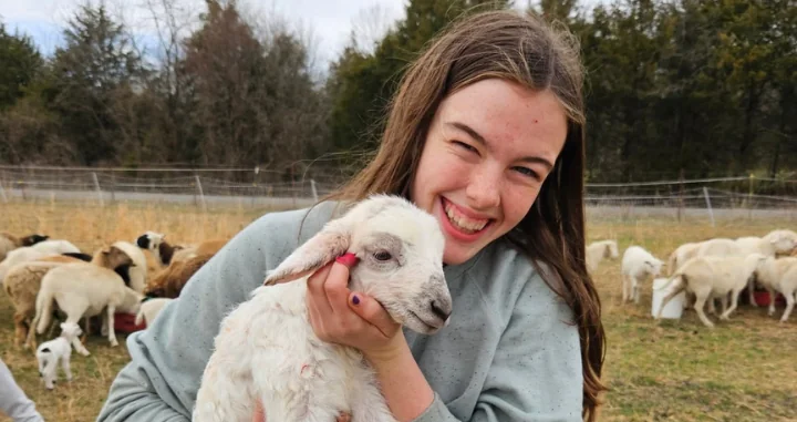 A farmer smiles holding a lamb.