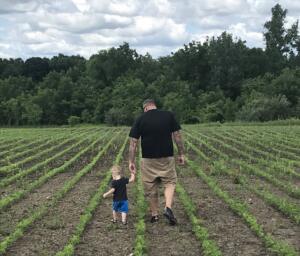 Farmer Alan Wilson walking through a field hand in hand with his son. 