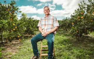 Ben McLean Sitting on a stool in an orange grove.