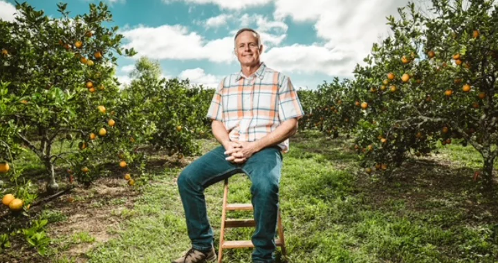 Ben McLean Sitting on a stool in an orange grove.